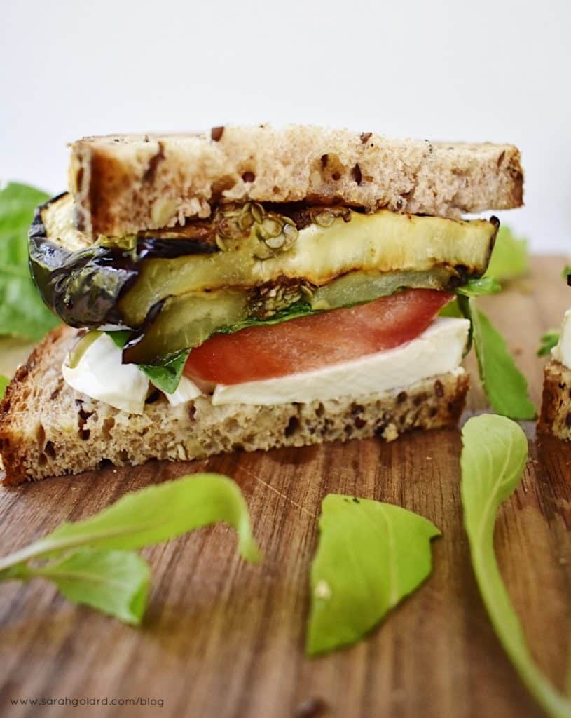 half of a grilled eggplant caprese sandwich with arugula on a wood cutting board