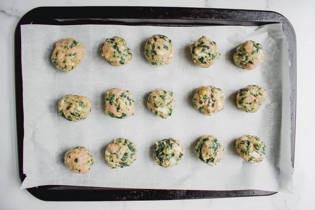 raw meatballs on a sheetpan with parchment paper.