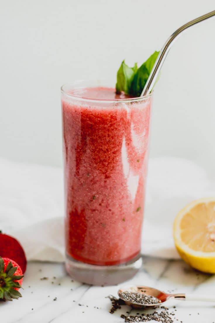 smoothie in tall glass with basil leaf and straw on marble background